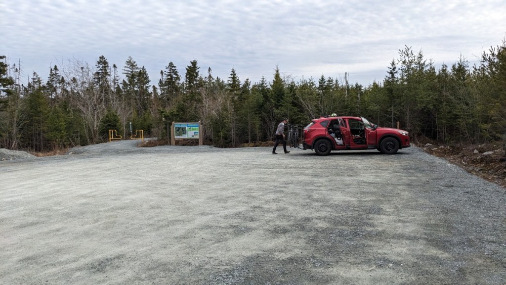 Large parking lot with only one vehicle. Large sign and trail entrance can be seen