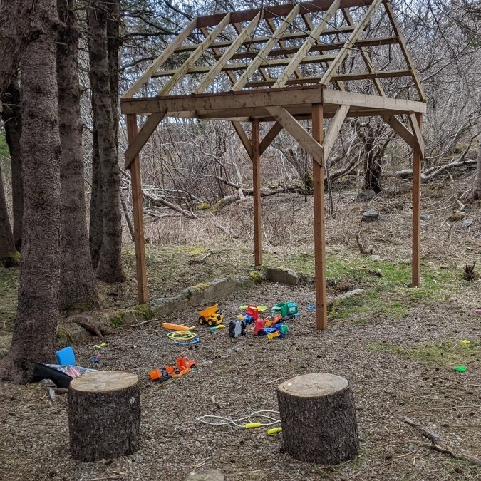 A simple roofed structure covering a play area with scattered toys.