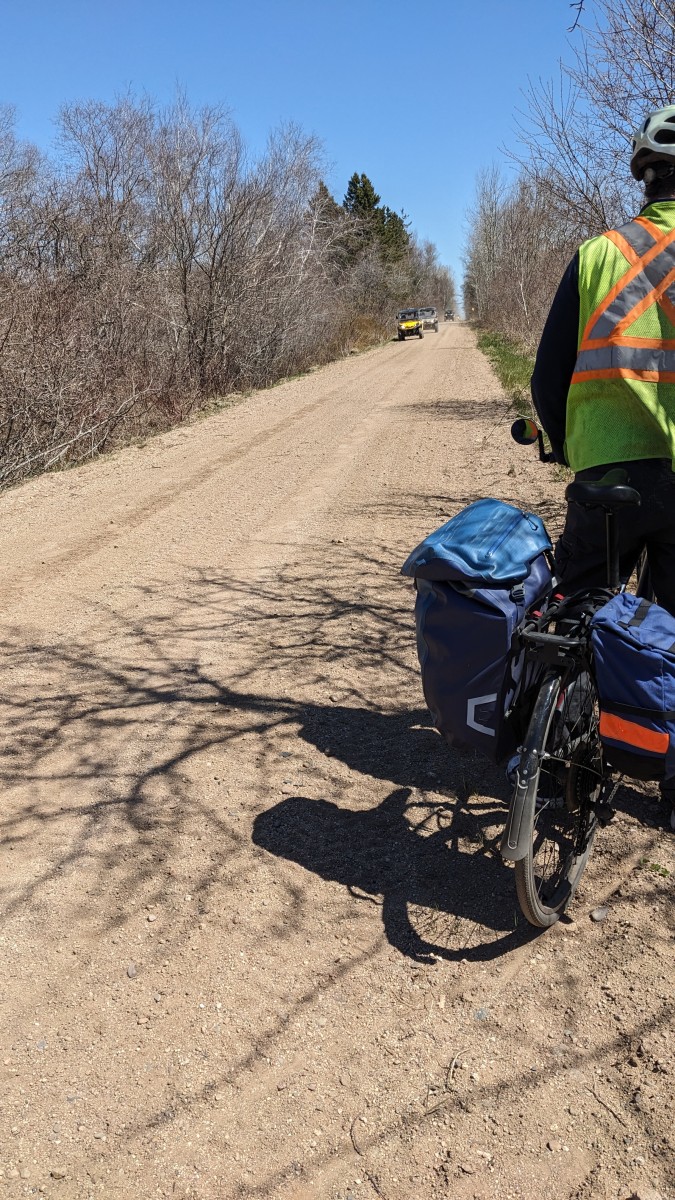 A cyclist on the side of a trail waiting for three ATVs to pass. The ATVs are coming towards the cyclist.