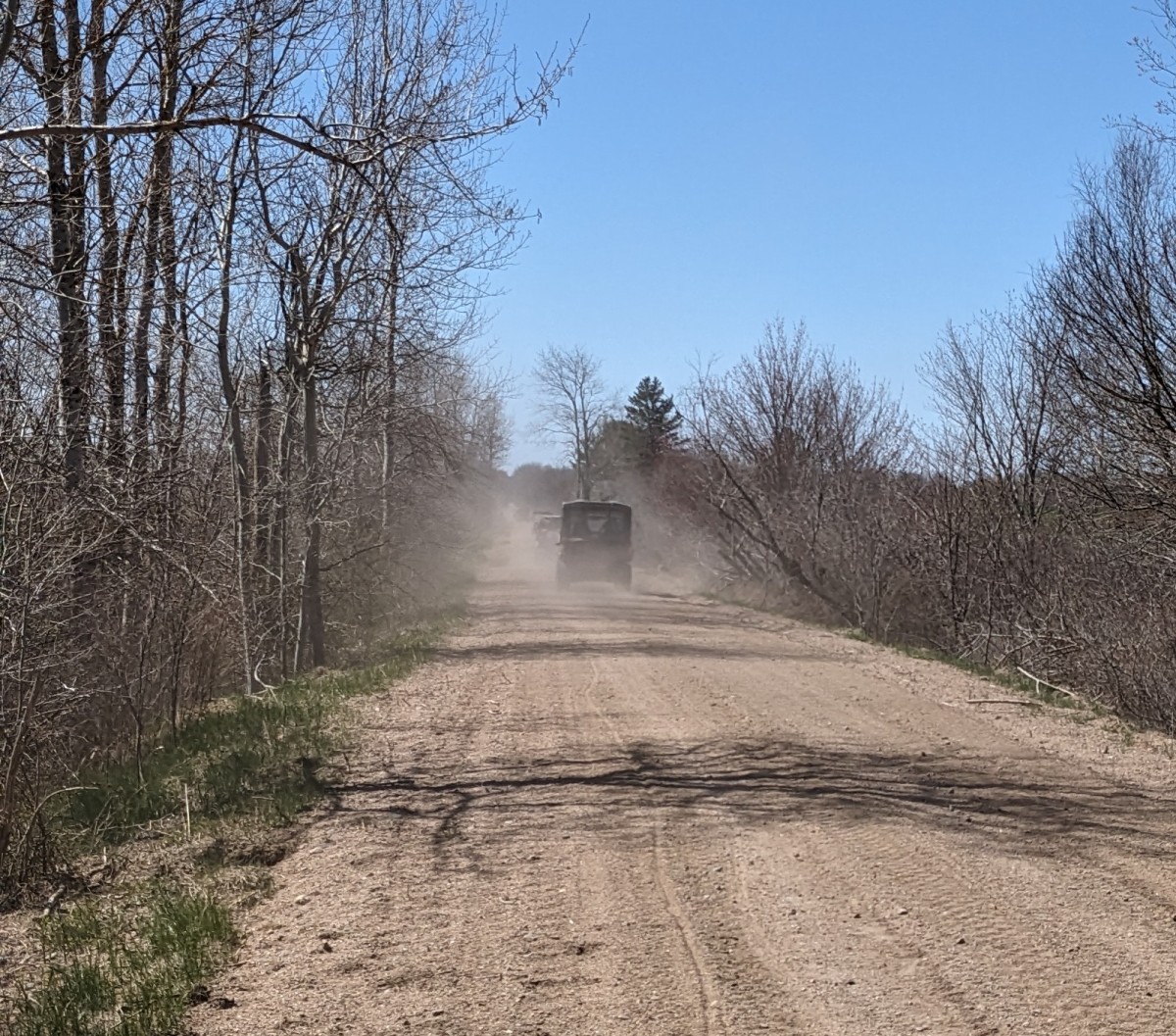 A trail with at least 4 ATVs in the distance. There is a lot of dust behind the ATVs.