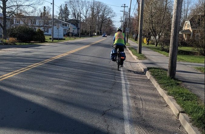 Cyclist riding on a road that has a shoulder that is covered in gravel and glass