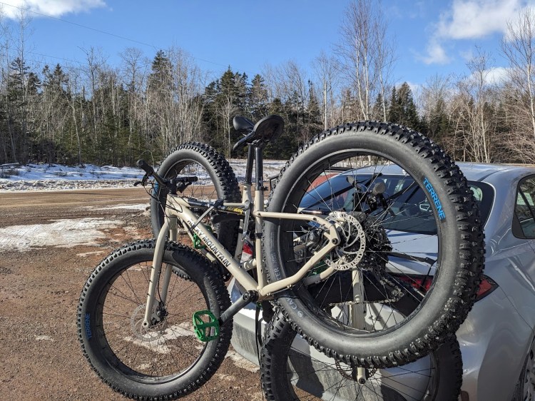 Two bicycles with oversized tires are strapped onto a bicycle rack that is hanging from the back of a car.